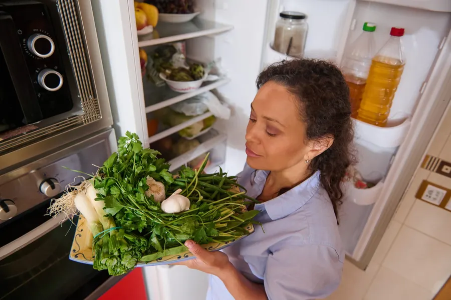 A homeowner taking fresh vegetables from an open refrigerator