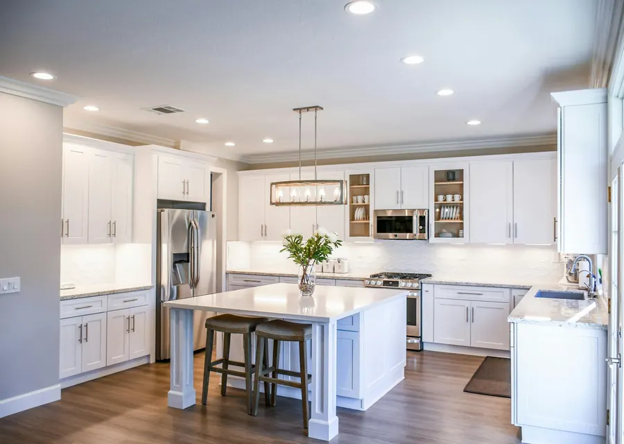 A white kitchen with an island, pendant lights, and stainless appliances